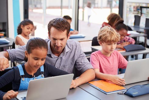 Male teacher helping a student learn on a laptop