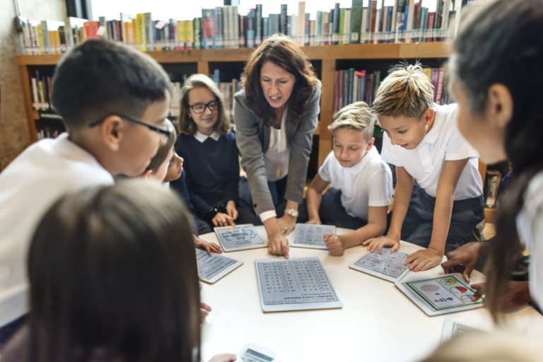 Teacher around a table with students and tablets.