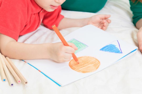 Young boy drawing shapes with colored pencils on white paper