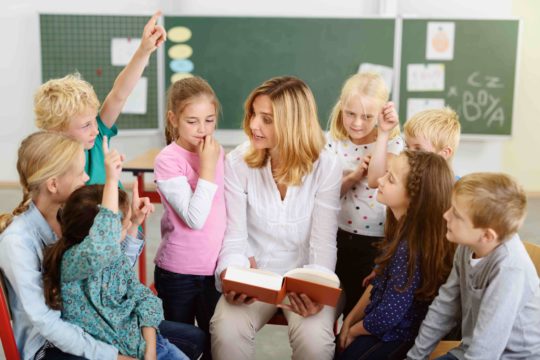 Female teacher reading a book to a group of young students