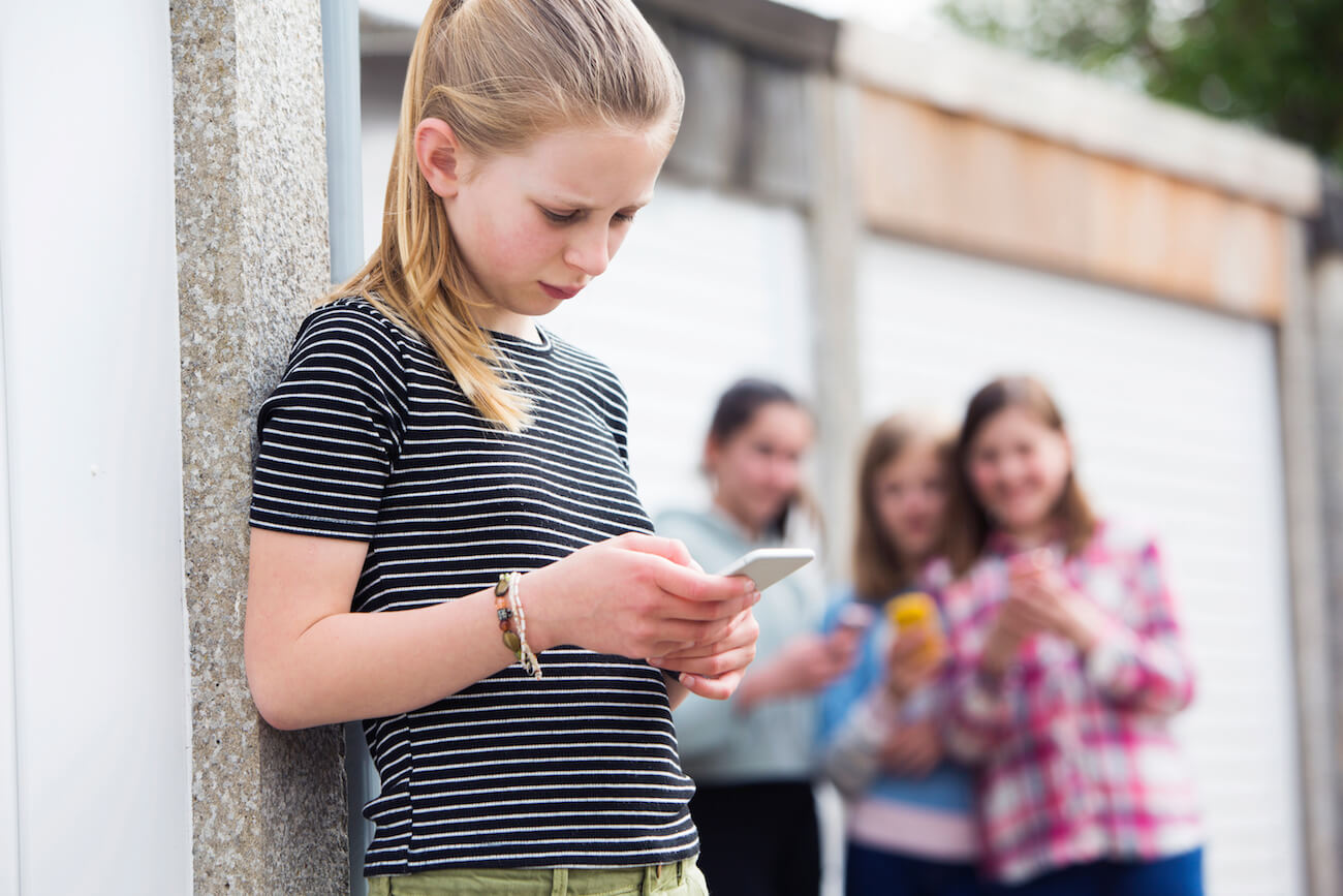 Upset young girl looking at her phone while other students watch