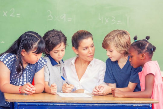 Teacher sitting at a table surrounded by students.