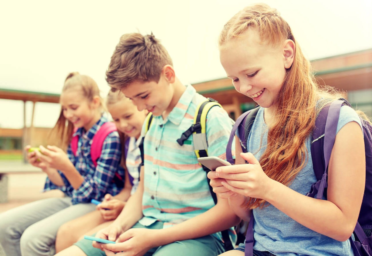 Smiling young students sitting outside looking at their cell phones