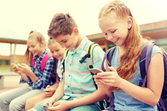 Smiling young students sitting outside looking at their cell phones