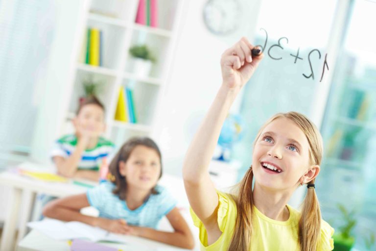 Young girl smiling while writing a math problem on smart board