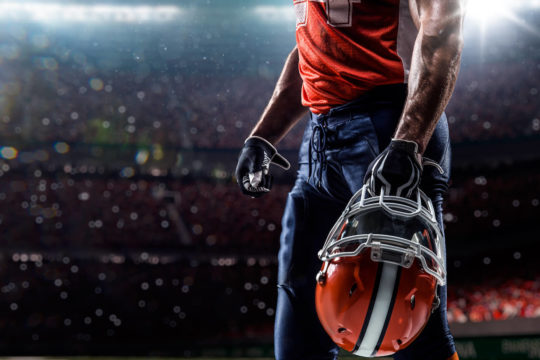 Football player in stadium holding helmet