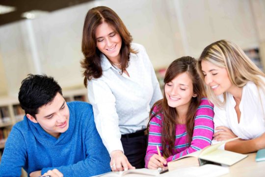 Female teacher helping a group of students writing