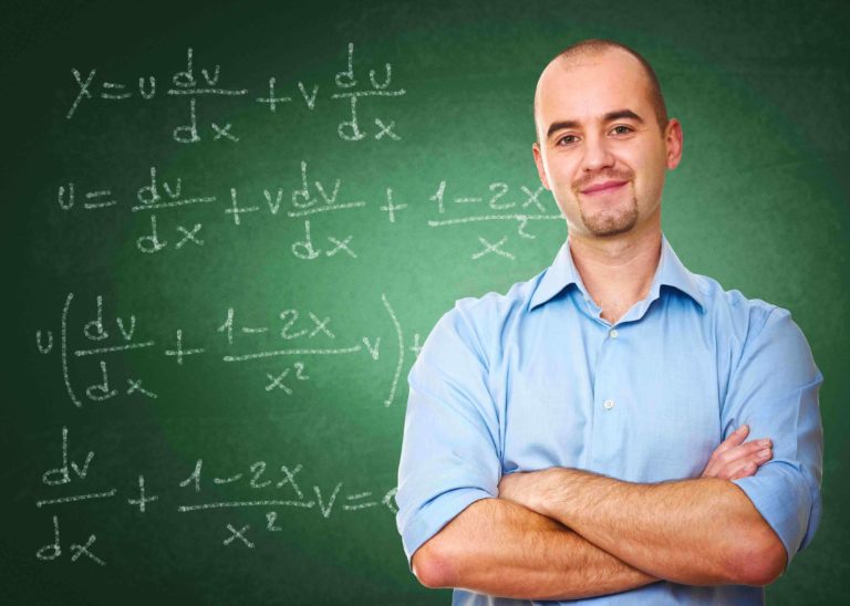 Male teacher with arms folded standing in front of a chalk board