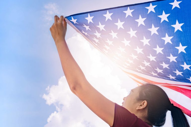 Young women holding a flag above her outside.