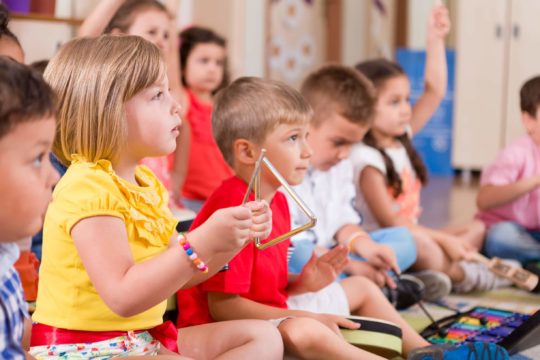 Young children sitting in a classroom with instruments.