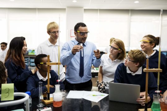 Teacher demonstrating a chemistry experiment to a group of students in a classroom lab.