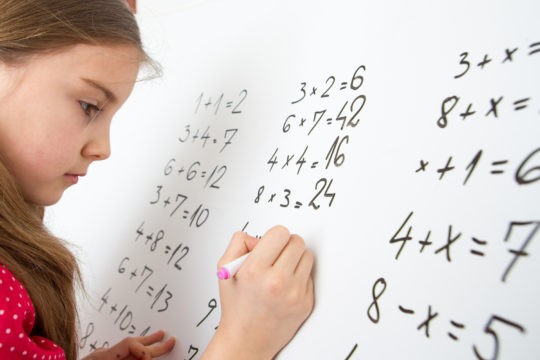 Young girl solving math problems on white board